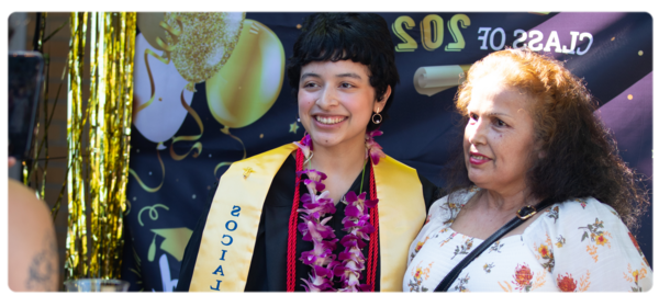 A graduating Social Work student stands with a parent in front of a Photo Booth backdrop